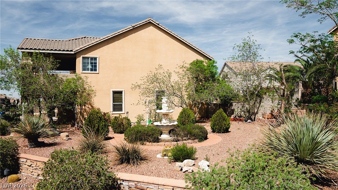 Side elevation of the home above a walled, terraced desert garden with a stone fountain